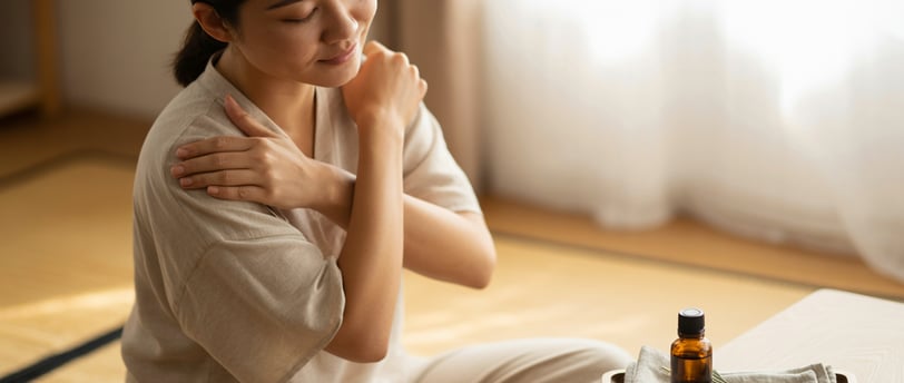 Người phụ nữ Việt massage vai thư giãn tại nhà với chai tinh dầu nhỏ, ánh sáng ấm áp