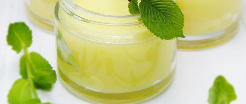 Potes de creme natural amarelo com folhas verdes e flores decorativas, representando cosméticos artesanais à base de ingredie