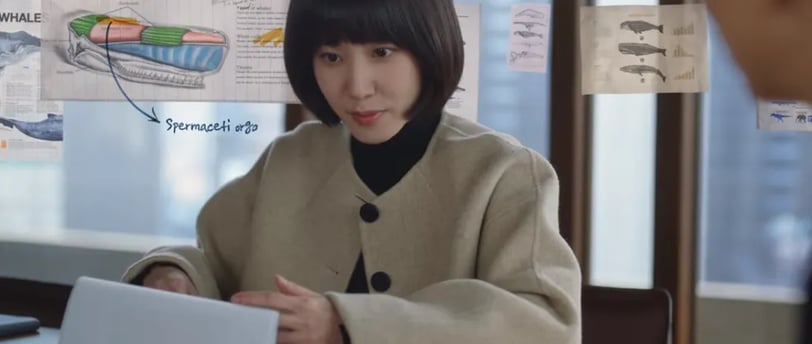 É a protagonista do Dorama (K-drama) Advogada Extraordinária segurando um papel na mão e pensando