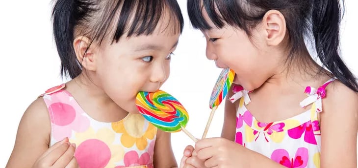 dua anak kecil yang sedang memakan permen
