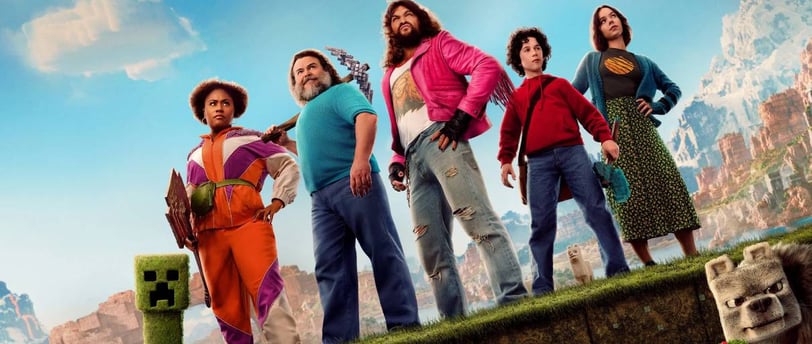 Minecraft movie cast posing with Creeper and wolf in colorful landscape inspired by the game world.