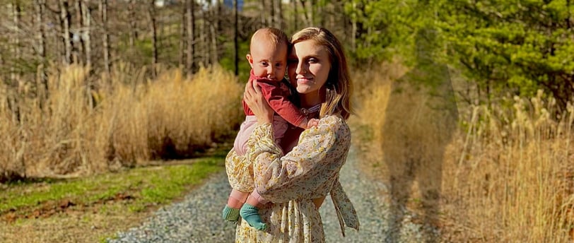 A mother holding baby on a gravel road at dusk, with the shadow of the father looming behind—tension of co-parenting & abuse 