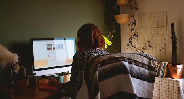 a woman sitting at a desk with a blanket draped over her