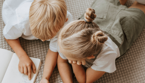 two kids laying on floor and writing