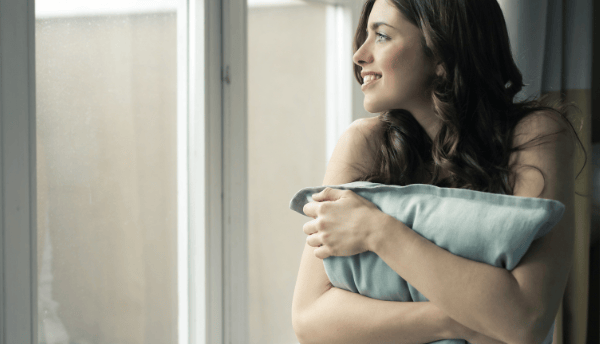 a girl sitting beside window and holding pillow