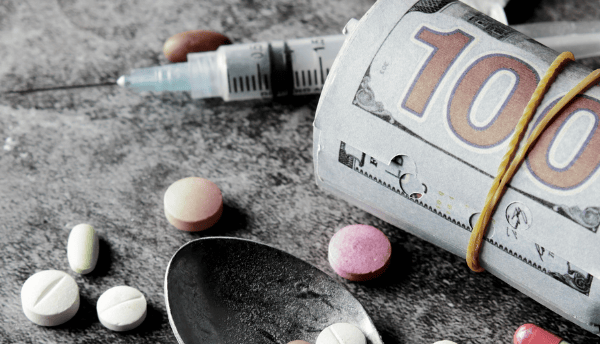 a spoon has tablets and a syringe and a bundle of cash
