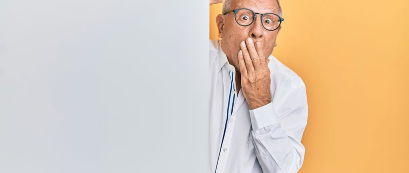 a man with glasses and a white shirt peeking out from the wall with a surprised expression.