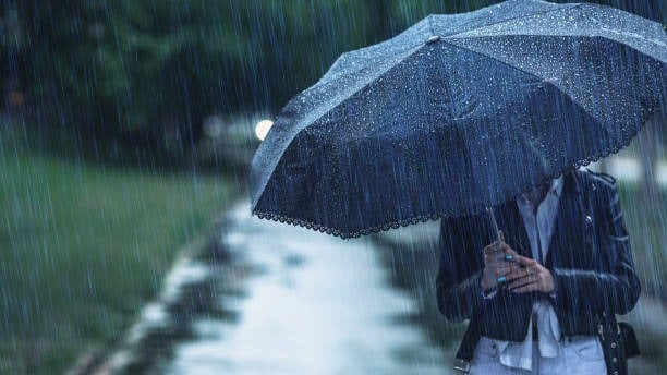 a man in a black jacket and white pants holding a black umbrella