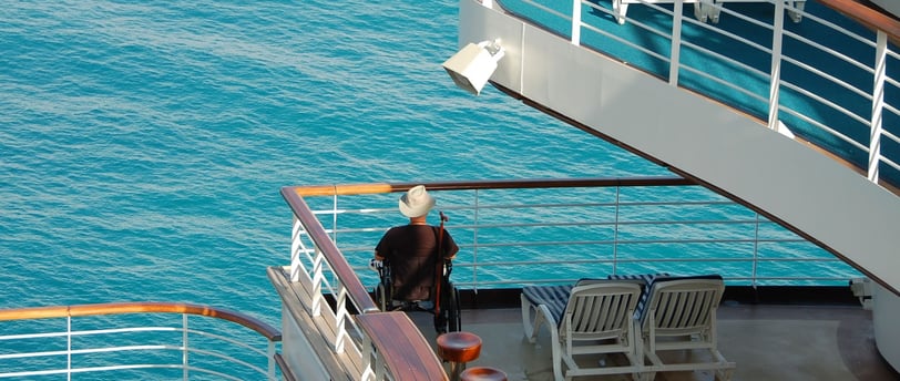 Passageiro em cadeira de rodas na varanda do navio, admirando a vista durante a navegação.