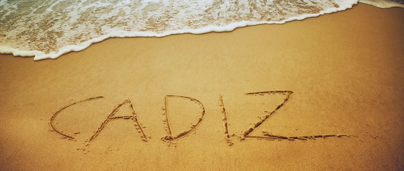 Foto de "Cádiz" escrito na areia da praia, com as ondas do mar ao fundo.