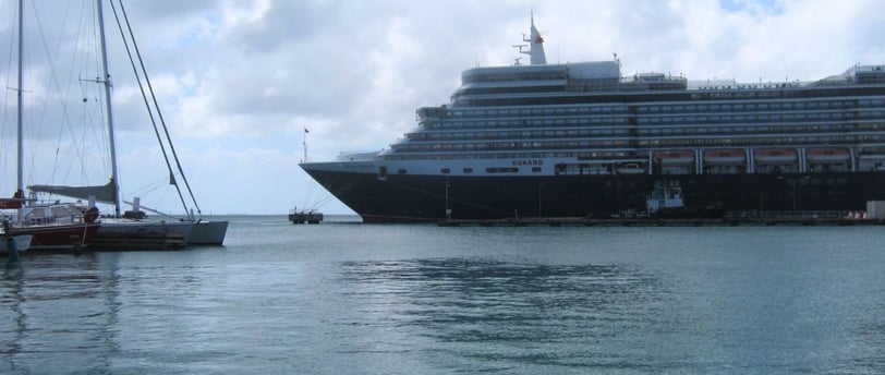 Navio de cruzeiro ancorado no porto de Oranjestad em um dia nublado, com a cidade ao fundo.