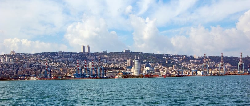 Navio chegando ao porto de Haifa visto do convés, com a cidade se estendendo ao pé do Monte Carmelo.