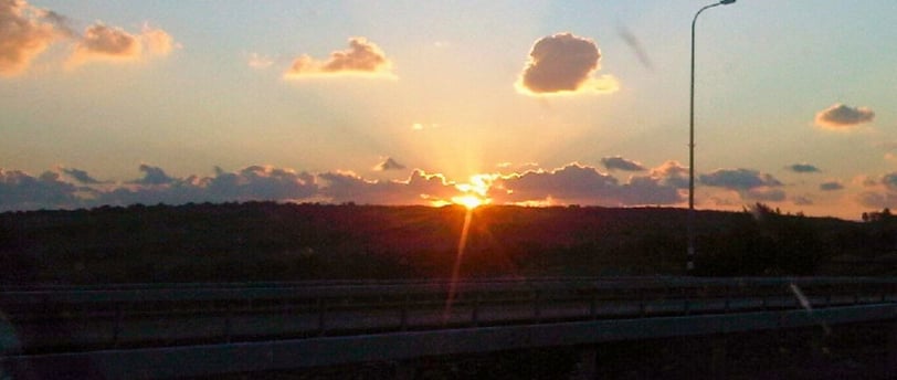 Volta de carro ao entardecer, despedida de Nazaré com o pôr do sol iluminando a estrada.