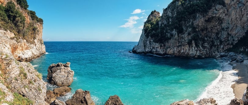 Vista da praia de Fakistra, em Vólos, na Grécia, com águas cristalinas e falésias ao redor.