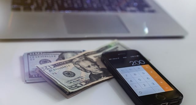 U.S. $10 and $20 dollar bills with a calculator app displayed on an iPhone next to it.