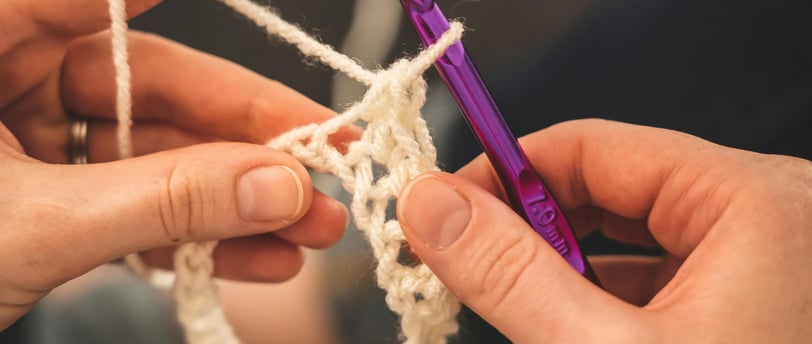 Des mains utilise un crochet de couleur violet pétant de taille de 7.0mm pour crocheter du fil