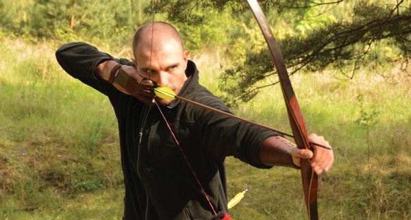 traditional archery technique a man in black shirt drawing a bow