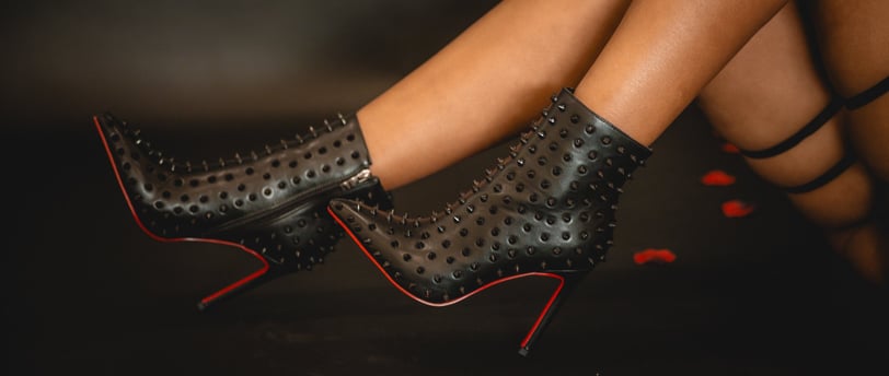 Close-up of a women's legs wearing black high-heeled ankle boots with pointed toes and decorative spikes.