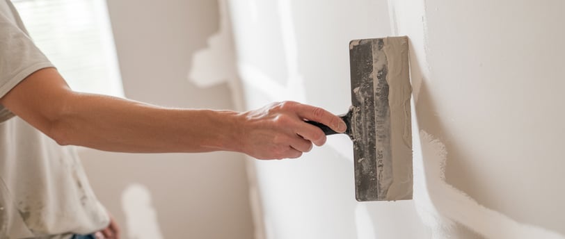 man applying drywall mud to a wall with a mud knife