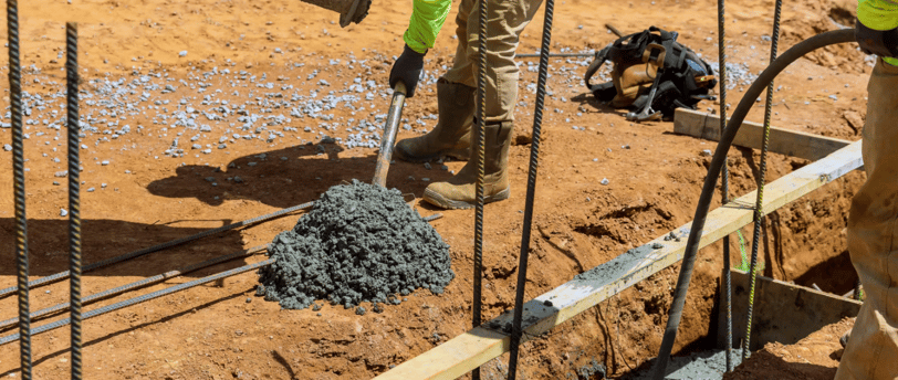 a man in a yellow jacket is pouring concrete into a concrete slab
