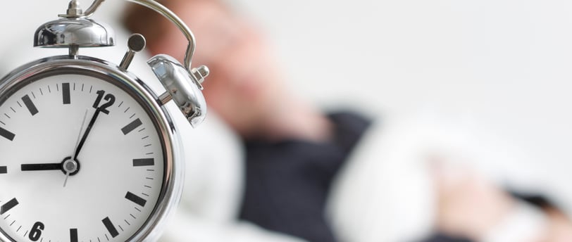 a man laying in bed with a clock on the side of the clock