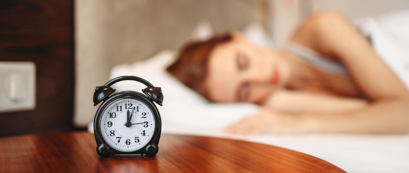 a woman is sleeping in bed with a clock