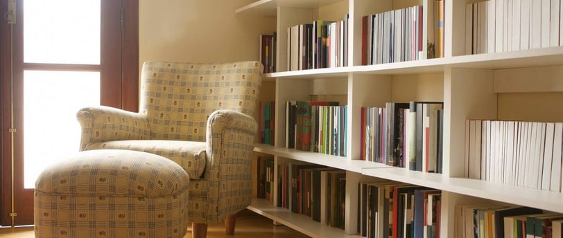 uma cadeira em frente a uma estante de livros ao lado de uma janela
