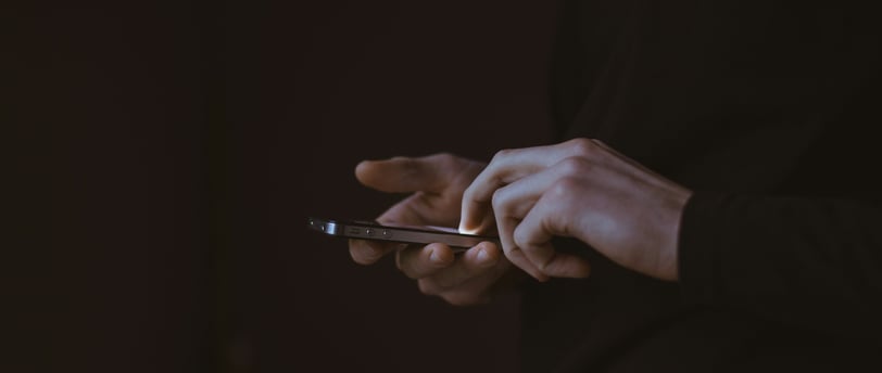A person wearing a dark long-sleeved shirt is using a smartphone in a dimly lit environment.