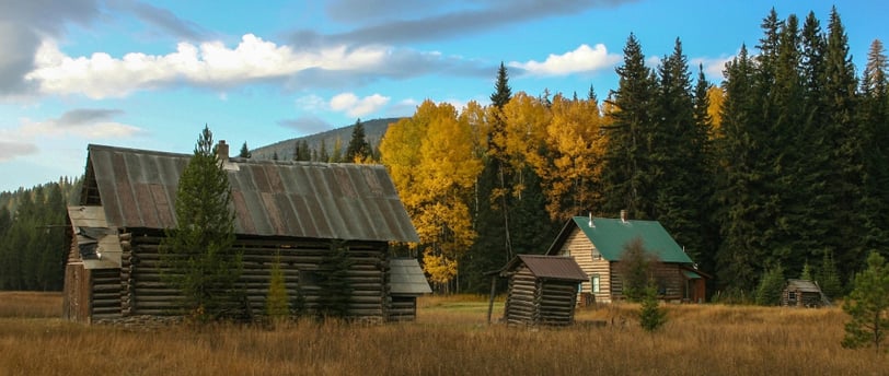 a log cabin in the woods with a blue sky and clouds