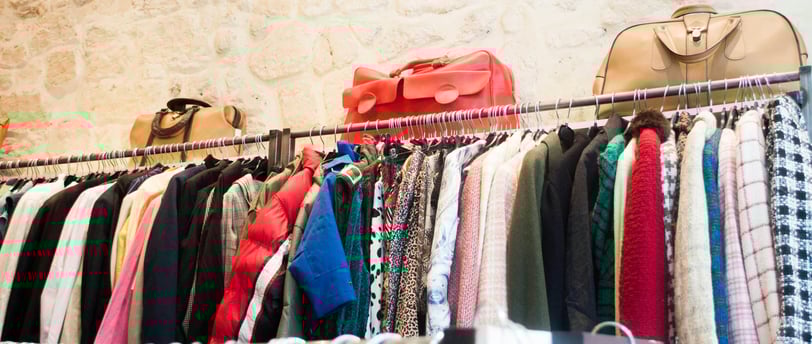 A full rack of long sleeve clothes with purses on top