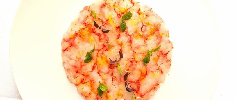Un plato blanco con un carpaccio de gambas en forma circular