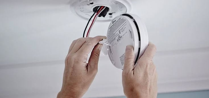 a person is holding a white smoke detector in their hands