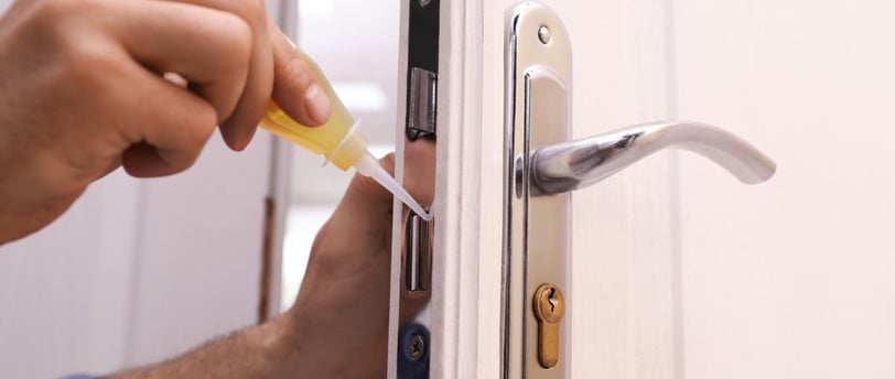 Hand applying lock lubricant to a door lock to prevent sticking and ensure smooth operation