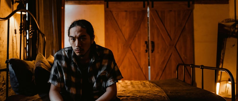 a man sitting on a bed in a bedroom contemplating relapse