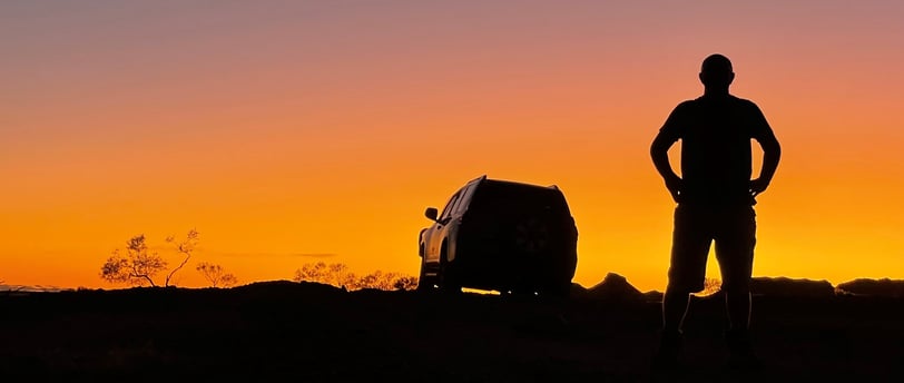 a man standing in the sunset with a car in the background