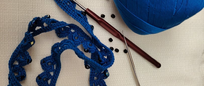 ouvrage bleu au crochet fin avec des perles noir et deux crochets le tout posé sur un fond crème 
