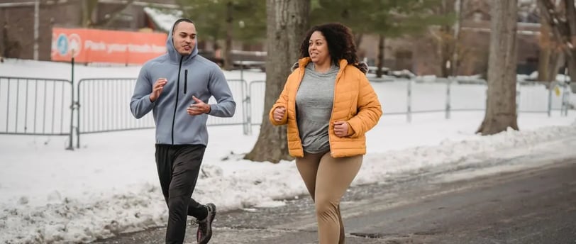 Plus-size woman jogging with a thinner man in the snow, showing real-life movement for weight loss in winter