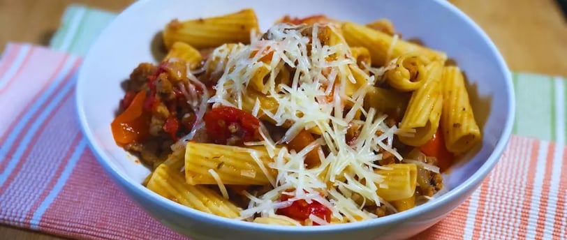 Italian sausage pasta skillet served in a white bowl with noodles on the table by a placemat