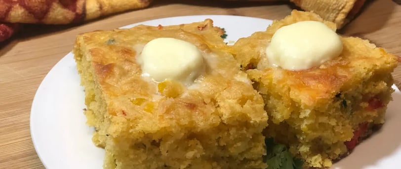 Two blocks of Mexican cornbread topped with pats of melting butter on a rustic plate