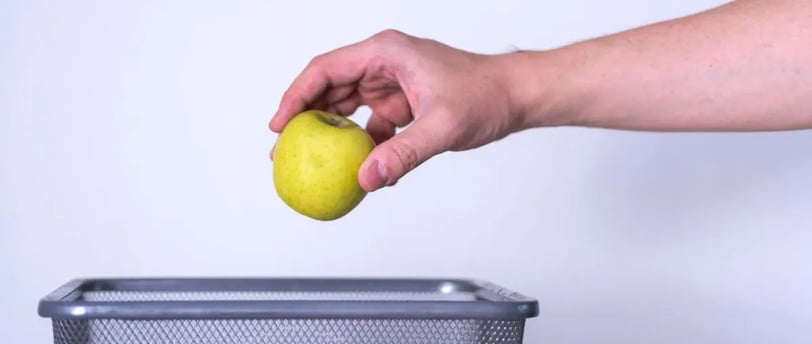Hand tossing spoiled apple into trash can