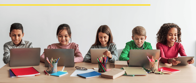 a group of children sitting at a table with laptops