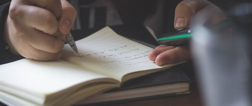 a person writing on a notebook with a pen and a pen