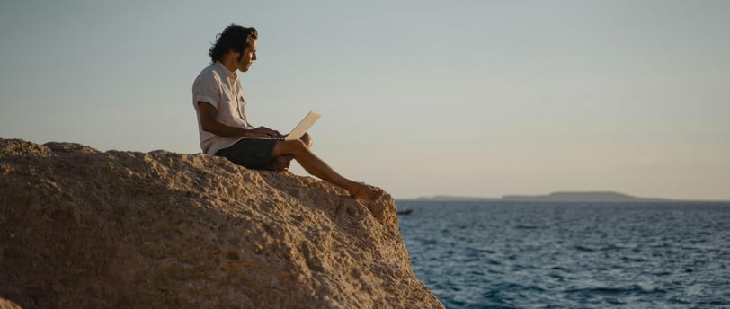 a man sitting on a rock with a laptop