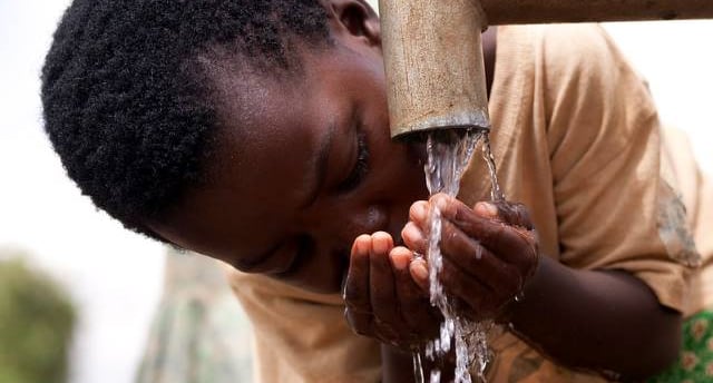 African child drinking clean water from a pipe with cupped hands