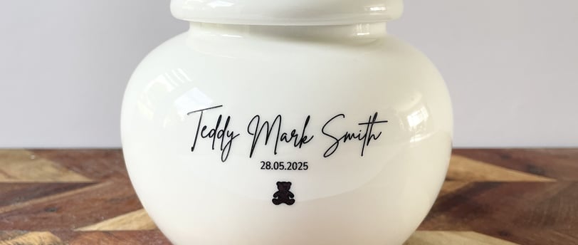 Elegant ivory ceramic urn with soft curves, engraved “Teddy Mark Smith” above a delicate black teddy bear icon.