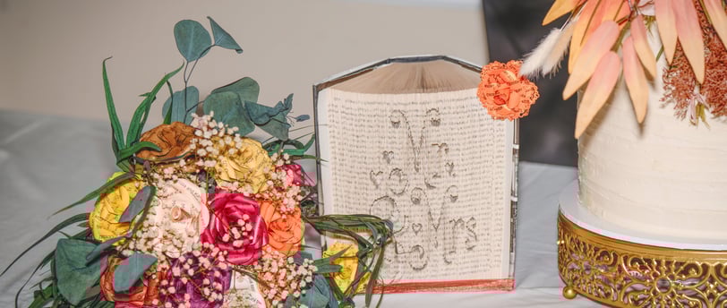 Bouquet of paper roses, Mr & Mrs carved into the pages of a Harry Potter book and wedding cake displayed on table