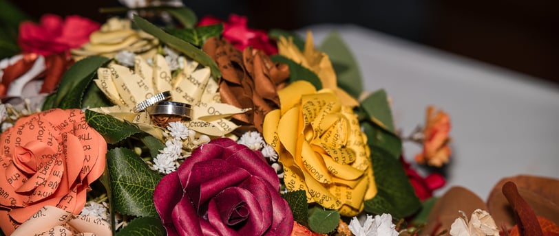 Beautiful bouquet of paper roses custom made with text quote on the flowers with the couples wedding rings resting on top