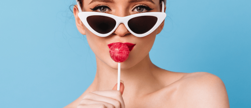 a woman with sunglasses and licking a lollipop