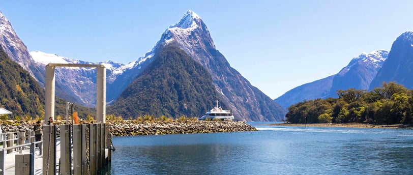 Mitre Peak reflecting in the tranquil waters of Milford Sound, surrounded by clear blue skies.