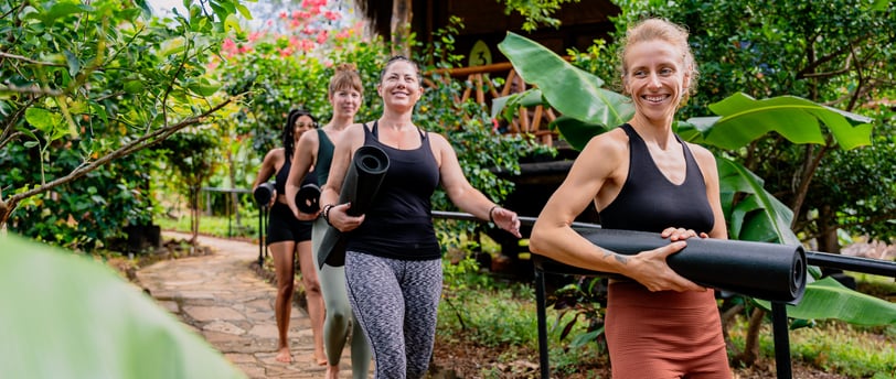 woman walking through tropical garden with yoga mat